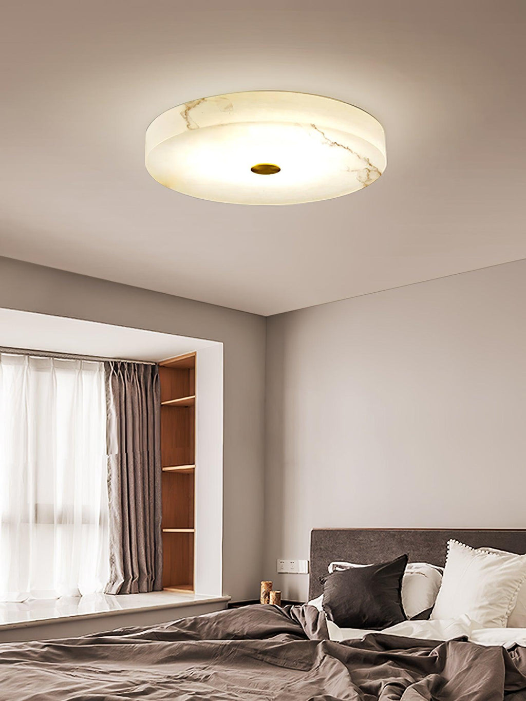 Closer view of the Olaean flush mount lit over a bed, the shallow alabaster drum seen edge-on.
