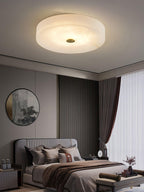 Large Olaean flush mount lit above a bed, round mirror and slatted wood panel on the wall behind.