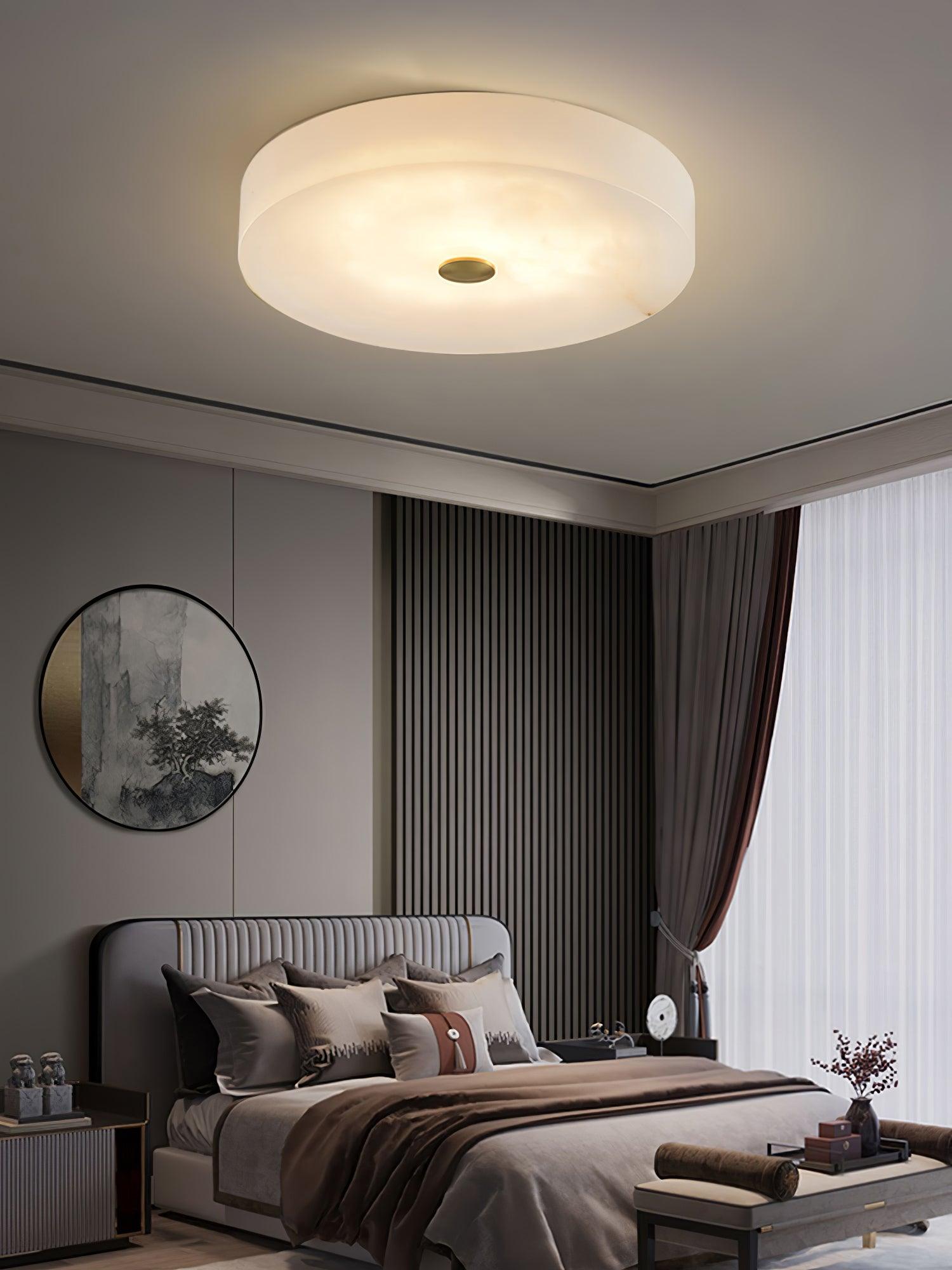 Large Olaean flush mount lit above a bed, round mirror and slatted wood panel on the wall behind.