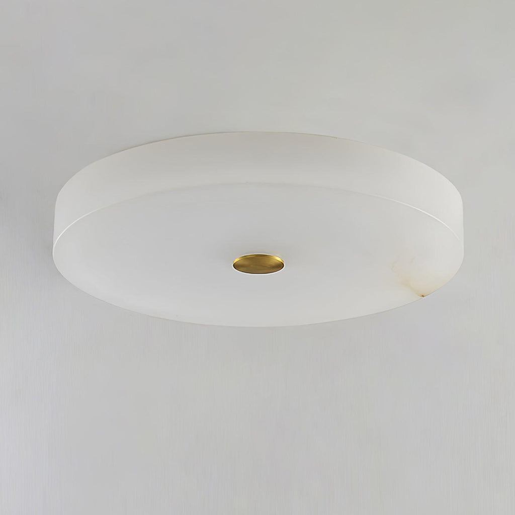 Unlit Olaean flush mount seen from below, brass cap flush with the flat alabaster underside.