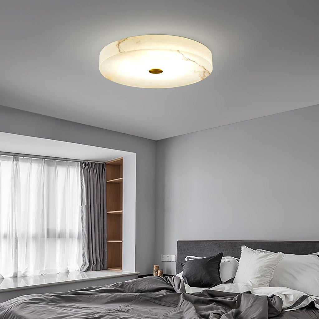 Olaean flush mount lit on a grey ceiling above a bed, natural veining visible in the stone.