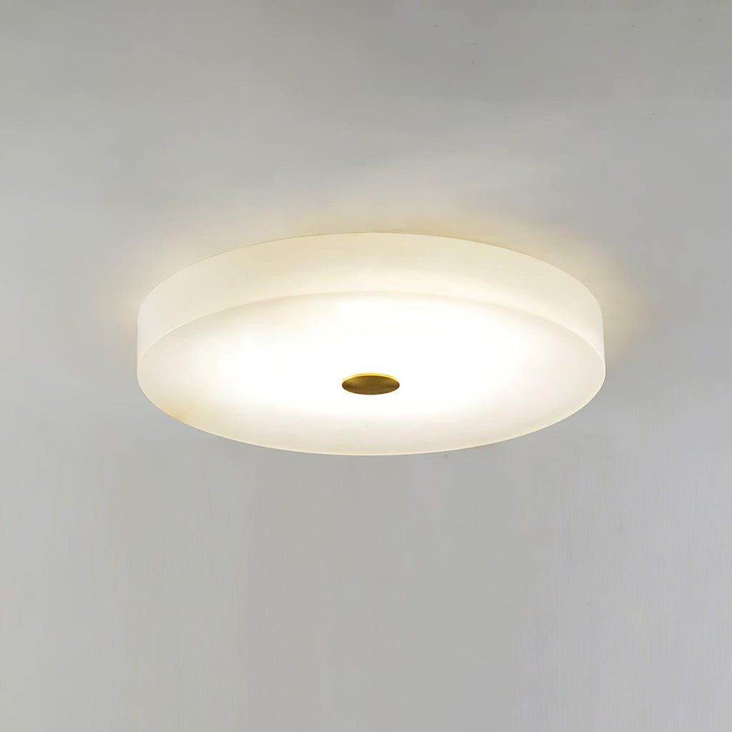 Olaean flush mount switched on against a bare ceiling, brass cap at the centre of the lit disc.