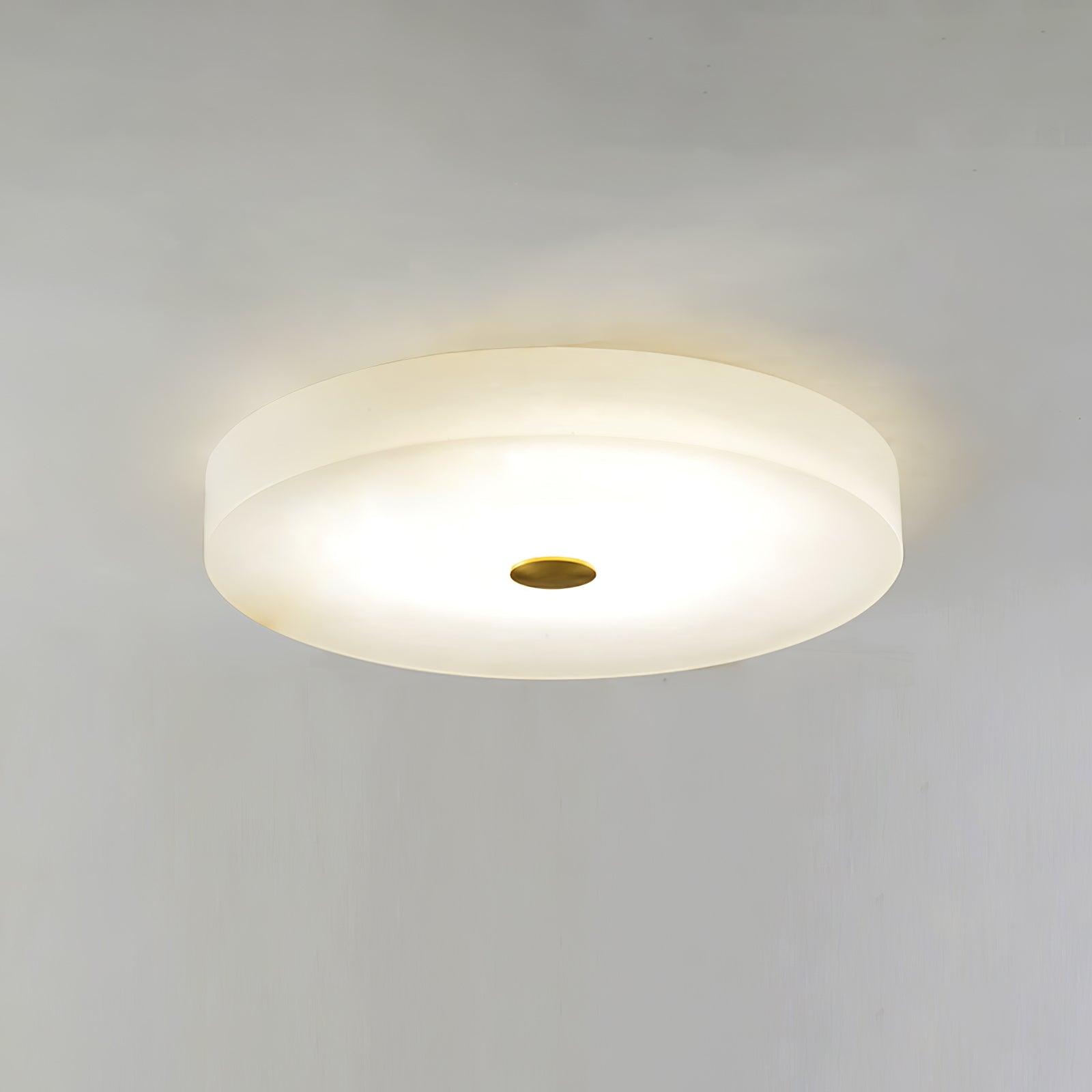 Olaean flush mount switched on against a bare ceiling, brass cap at the centre of the lit disc.