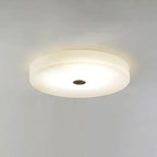 Olaean flush mount lit against a plain wall, its dark centre cap set in the glowing alabaster.