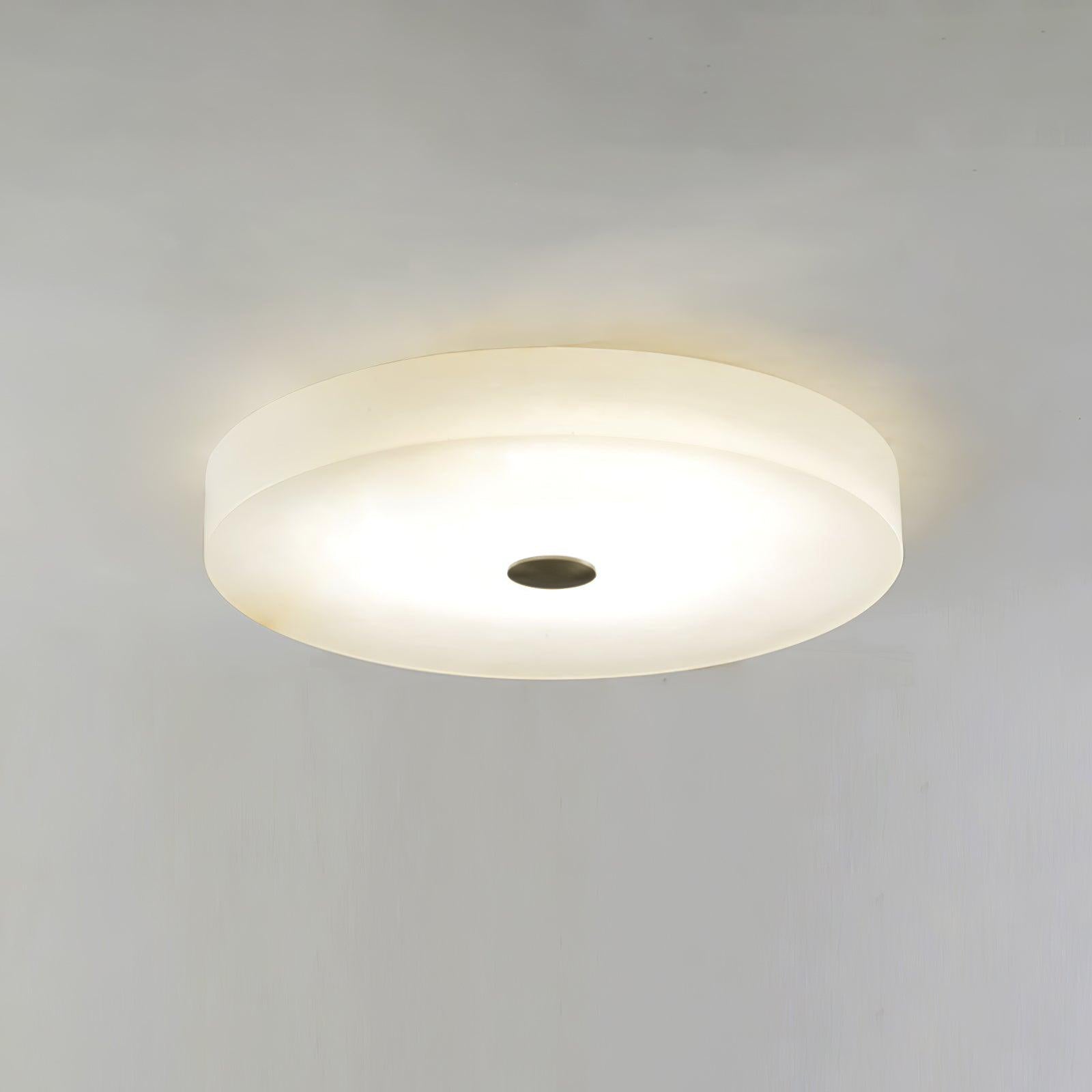 Olaean flush mount lit against a plain wall, its dark centre cap set in the glowing alabaster.