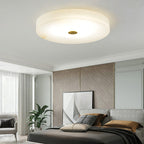 The Olaean flush mount lit in a bright bedroom with a leaning artwork and a potted plant.