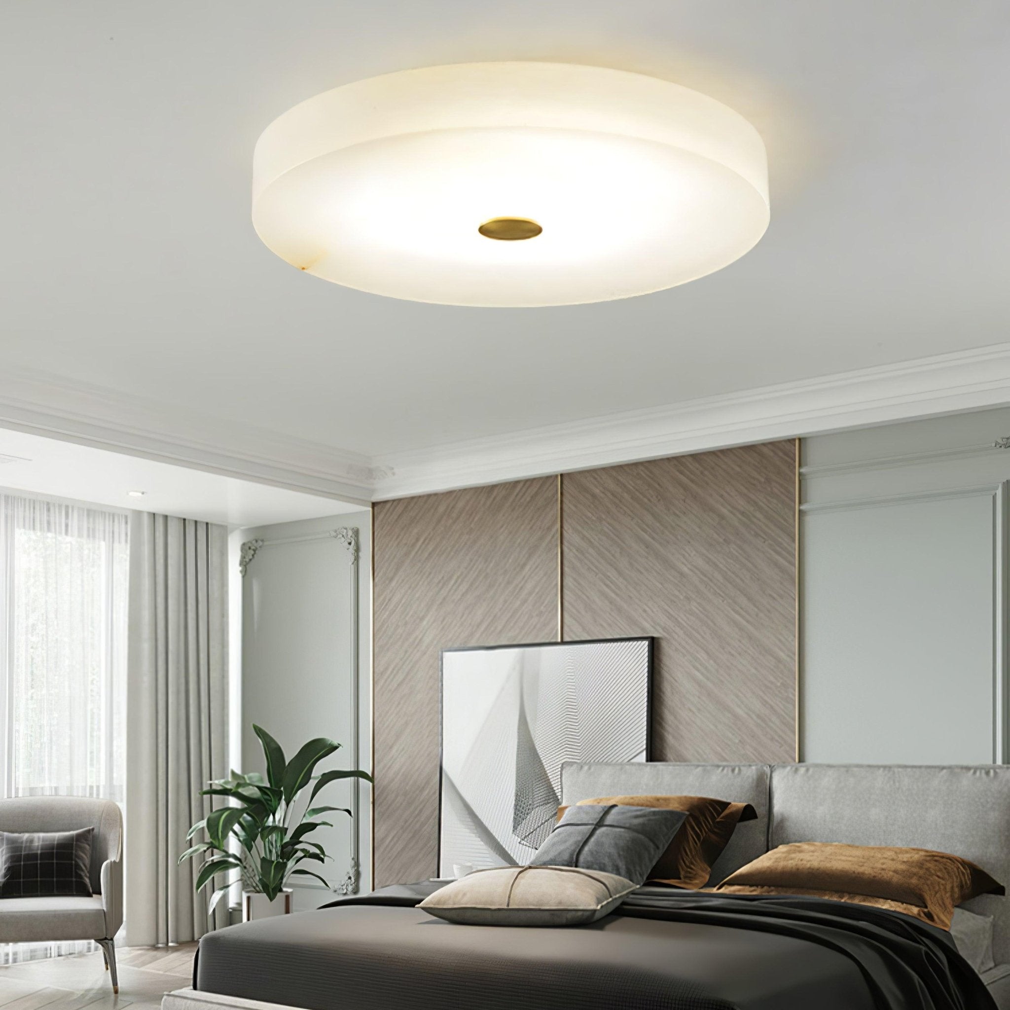 The Olaean flush mount lit in a bright bedroom with a leaning artwork and a potted plant.