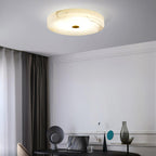 Olaean flush mount lit above a desk corner, veined alabaster glowing against a grey ceiling.
