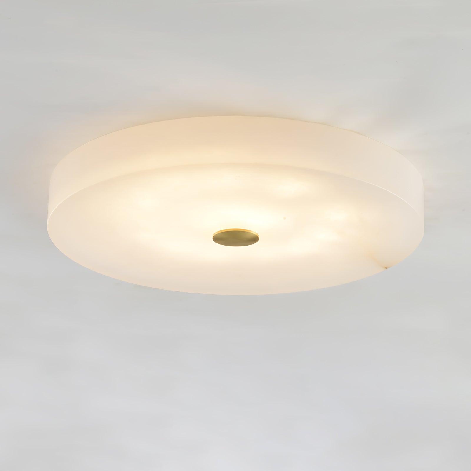 The Olaean flush mount with brass centre cap, its alabaster drum glowing warm against a white ceiling.