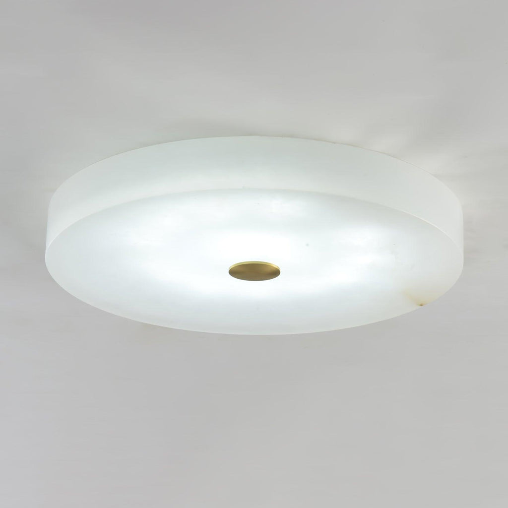 Olaean flush mount lit in a cooler white light, brass cap centred on the pale alabaster face.