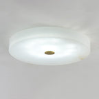 Olaean flush mount lit in a cooler white light, brass cap centred on the pale alabaster face.