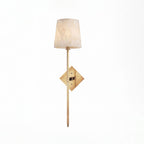 Lit on a plain white background, this Clérachic sconce's tall alabaster shade glows above its brushed brass diamond backplate.