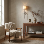Above a console table with dried branches, this Clérachic sconce in brushed nickel lights a wood-framed armchair with a cream throw.
