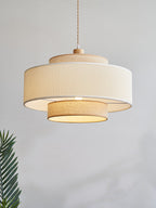 Against a plain grey backdrop, the white pleated band and beige drum of this Clérachic pendant catch the light, a palm leaf beside it.