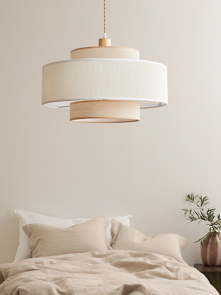 In this bedroom, a white pleated band tops the beige drum of this Clérachic pendant above a bed dressed in linen.