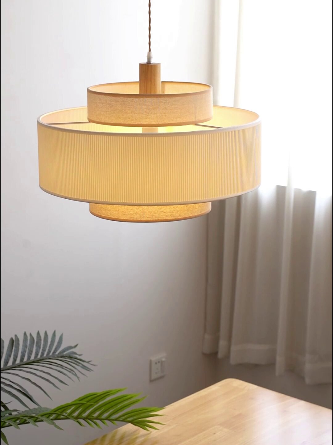 Close view of this Clérachic pendant's stacked drums beside a sheer curtain, a leafy plant in the foreground.