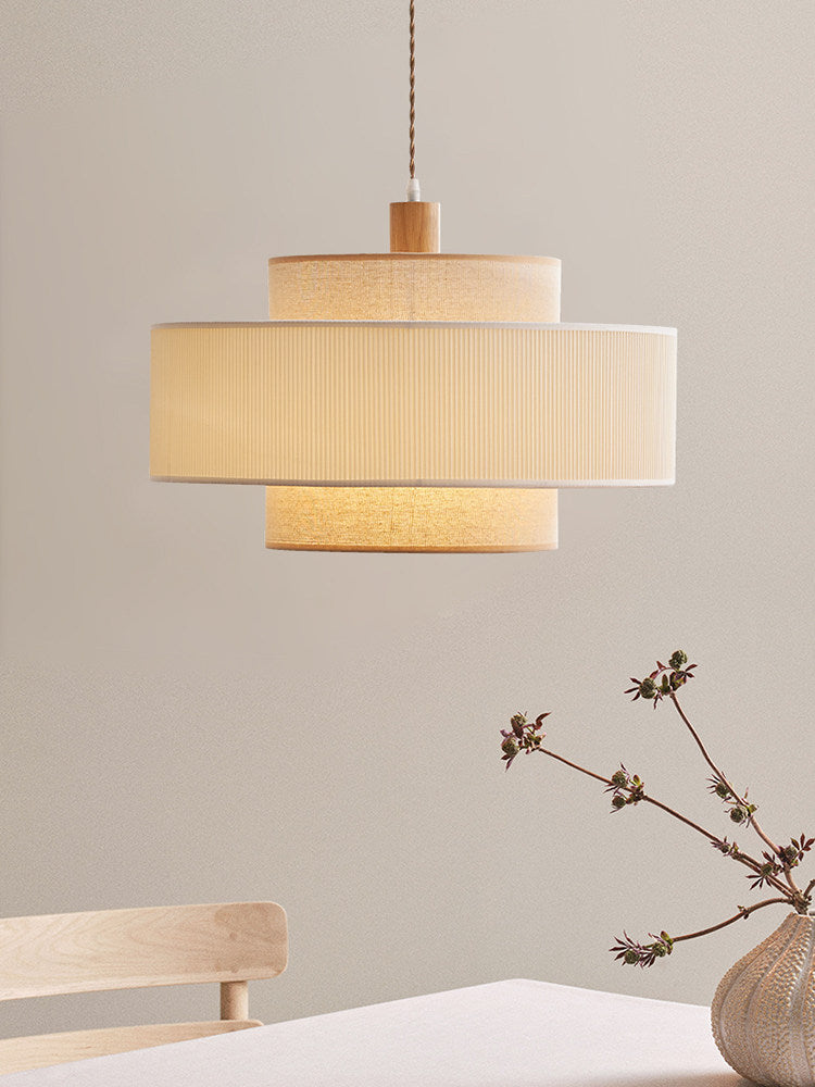 This Clérachic pendant hangs against a plain wall, a small dried branch in a vase on the wood surface below.