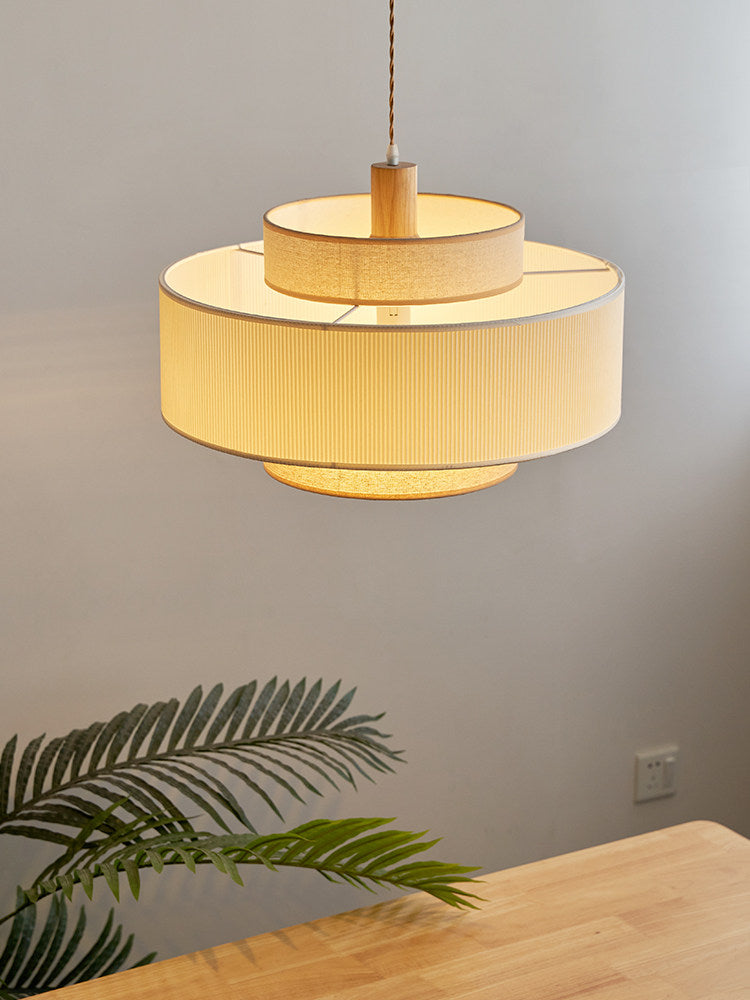 Lit warmly against a grey wall, this Clérachic pendant's tiers glow above a wood surface with a leafy plant nearby.