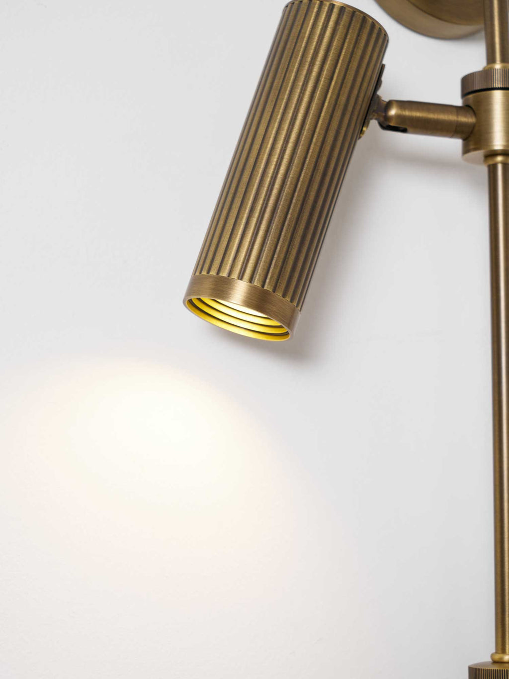 A warm glow spills from one ribbed head on this Clérachic plug-in spotlight in bronze finish, shown against white.
