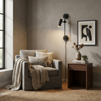 This Clérachic plug-in spotlight in black finish lights a grey armchair with cushions and a folded throw.
