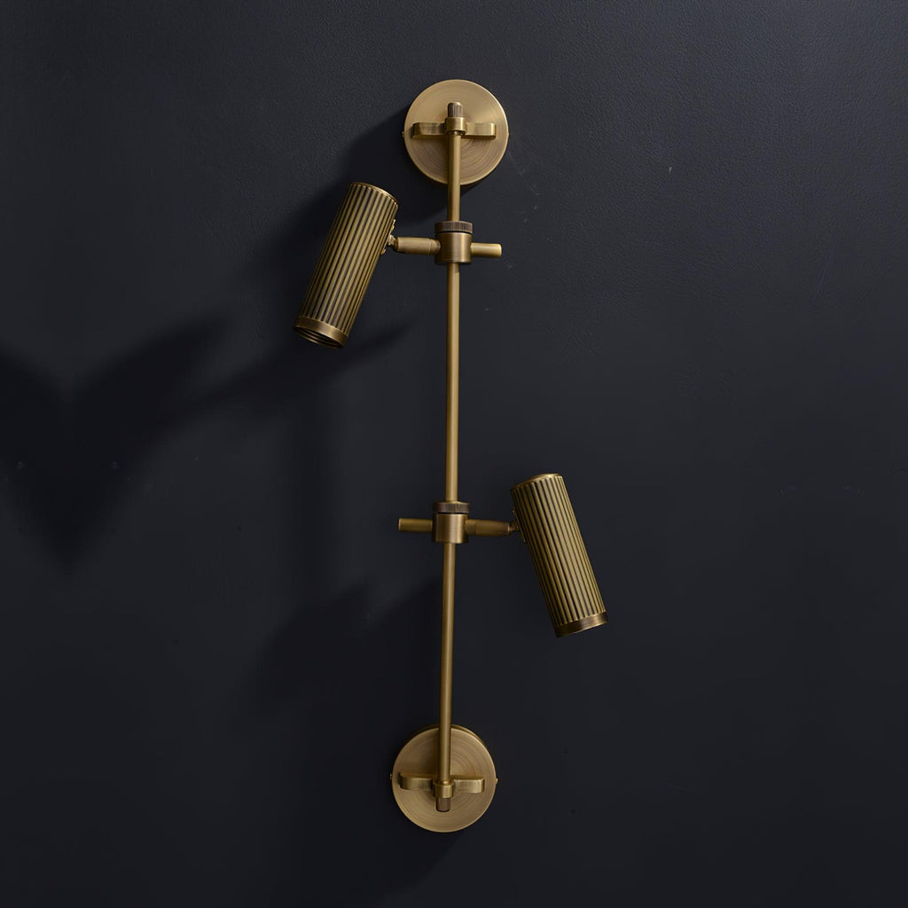 Both ribbed heads angle outward on this Clérachic plug-in spotlight in bronze finish, against a dark wall.