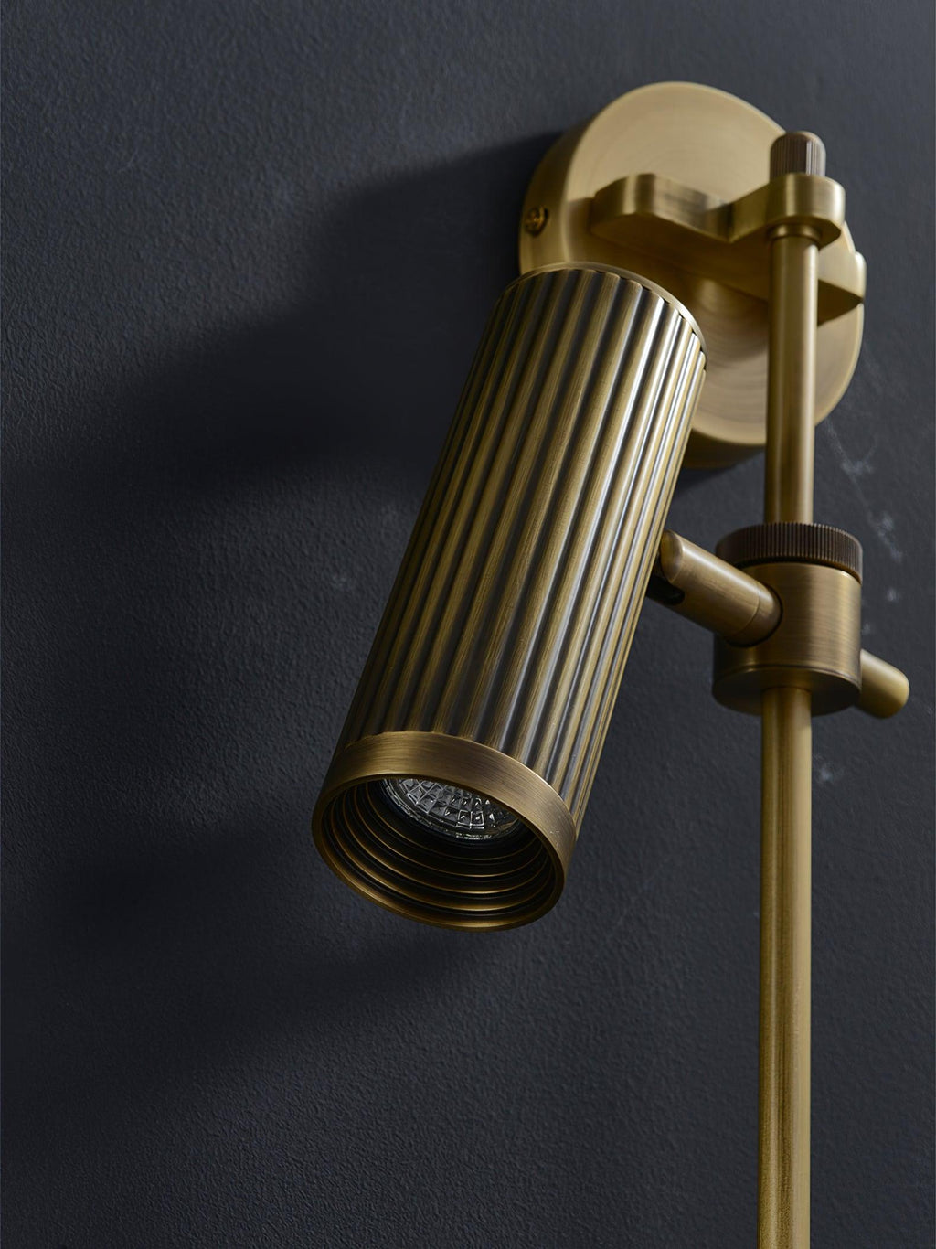 Close view of this Clérachic plug-in spotlight in bronze finish against dark, its head angled toward the wall.