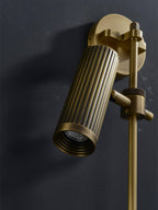 Close view of this Clérachic plug-in spotlight in bronze finish against dark, its head angled toward the wall.
