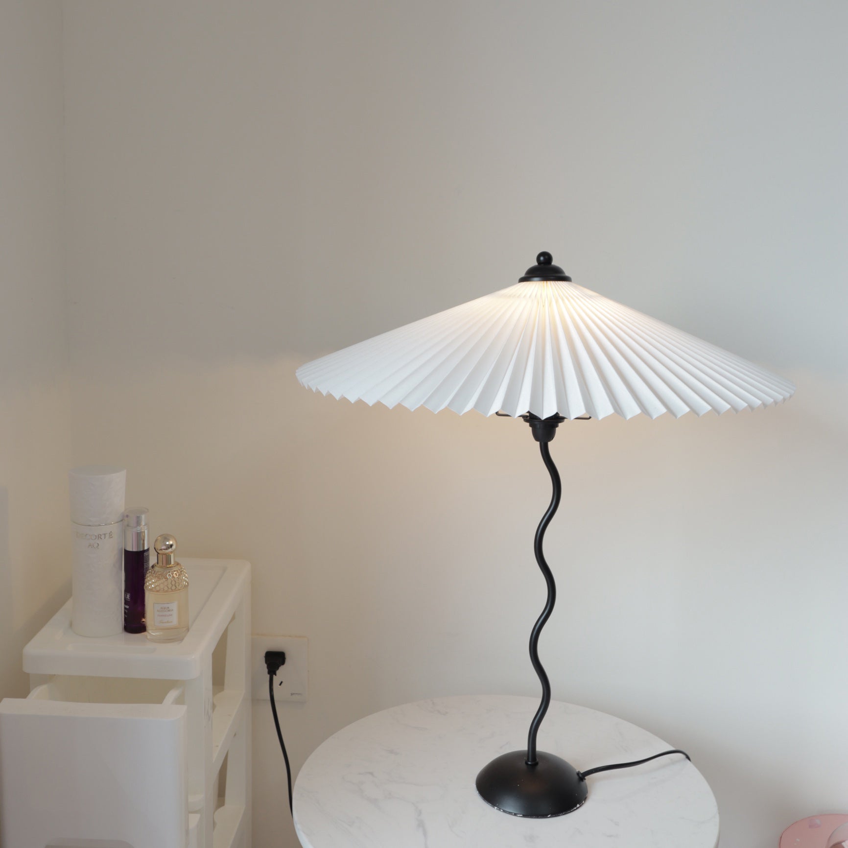 Squiggle table lamp pleated shade glowing on a side table