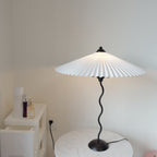 Squiggle table lamp with dark green pleated shade in a room