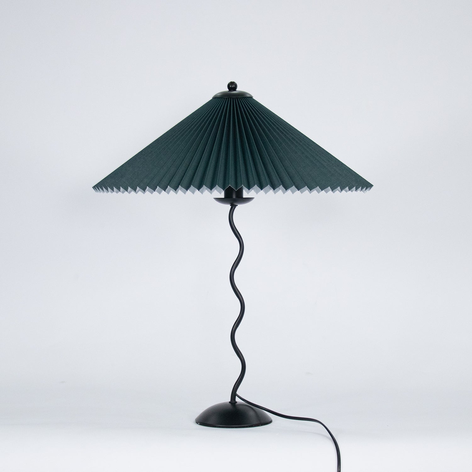 Squiggle table lamp glowing softly with pleated fabric shade