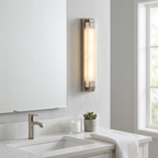 This Clérachic panel sconce in satin nickel finish is lit beside a mirror in a minimalist white bathroom.