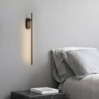 Slim stick-shaped wall sconce in brass casting a vertical glow
