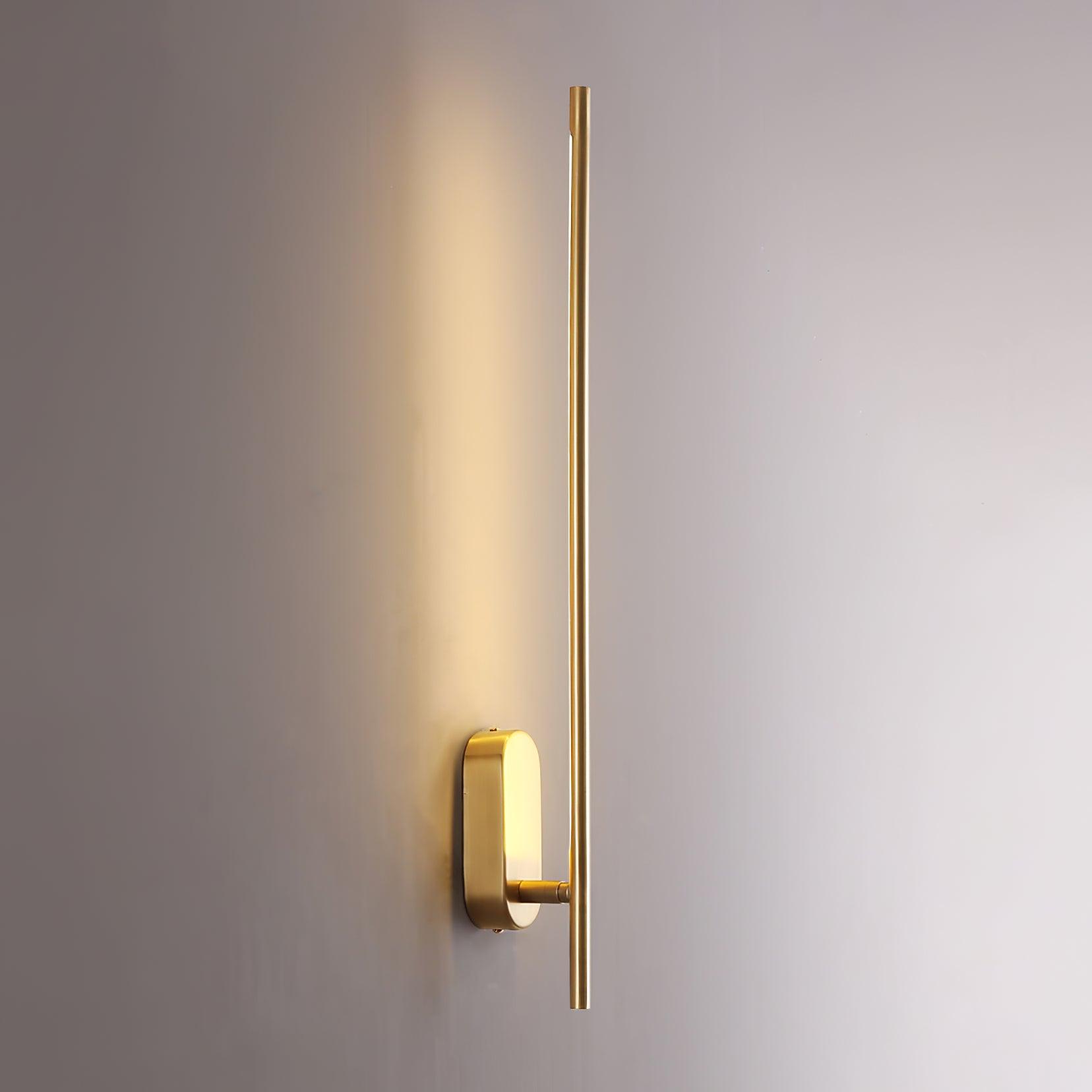 Stick-shaped sconce in brass mounted beside a mirror