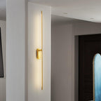 Brass stick wall sconce shown lit in a minimalist interior