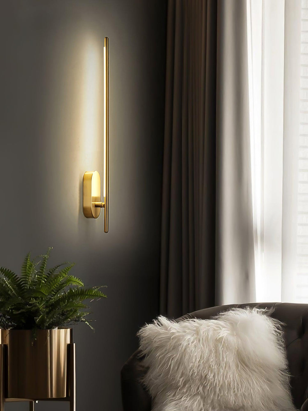 Brass stick wall sconce lit beside a comfortable armchair