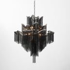 A black-chain Clérachic chandelier, lit, its scalloped tiers stepping outward against a plain white backdrop.