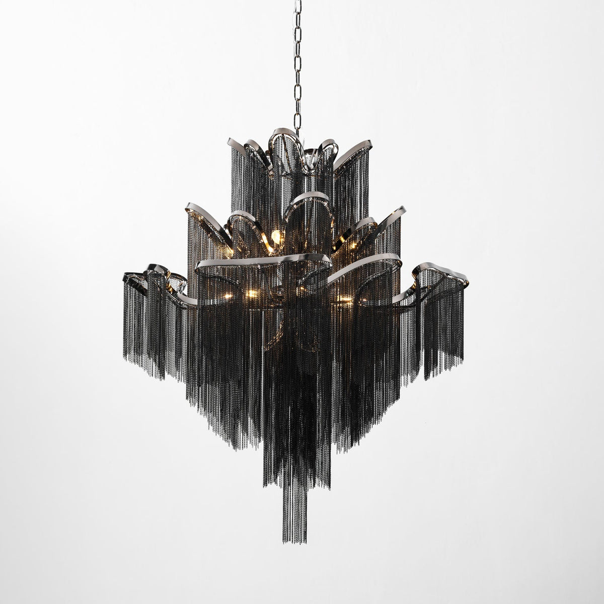 A black-chain Clérachic chandelier, lit, its scalloped tiers stepping outward against a plain white backdrop.