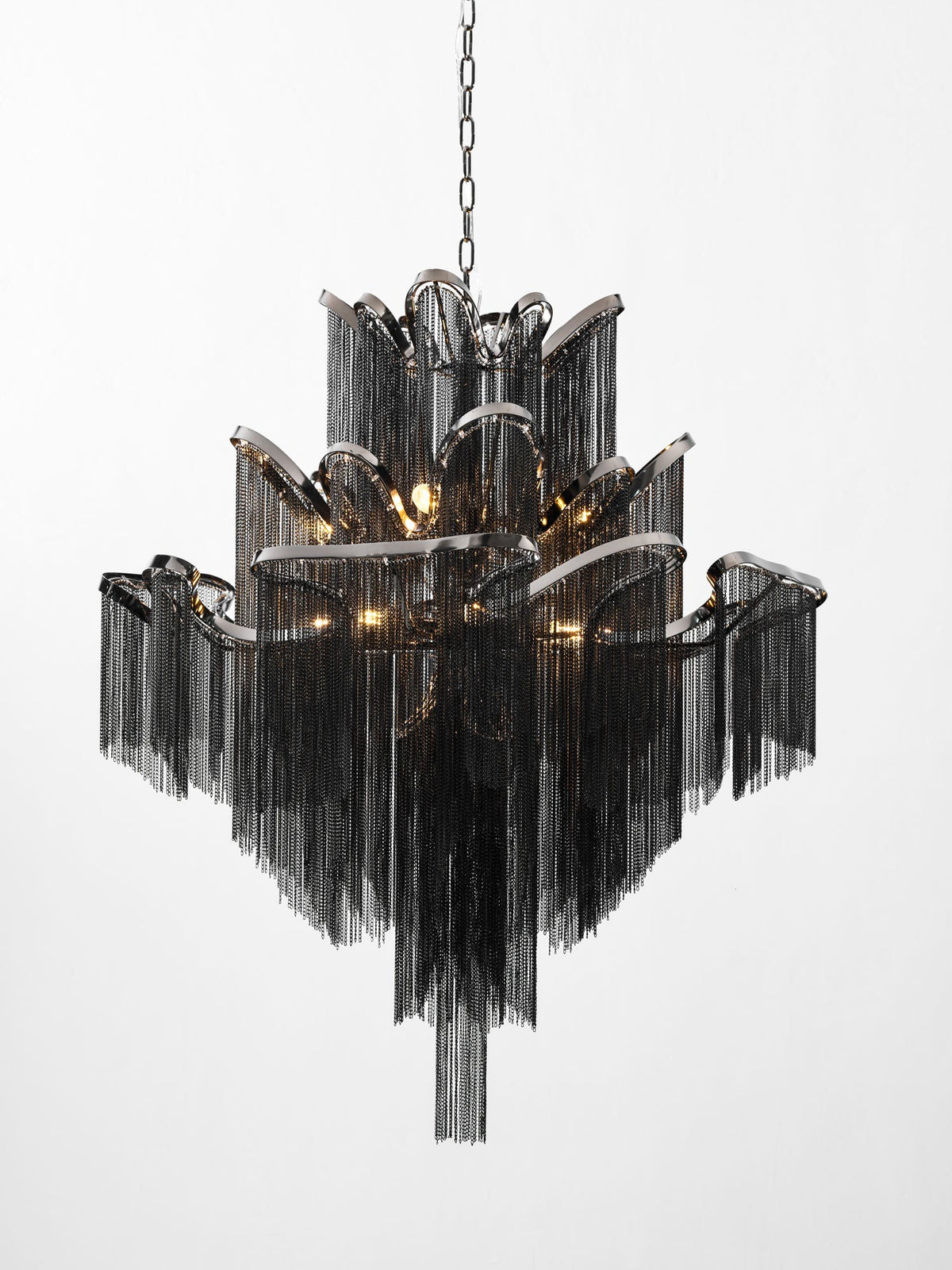 In black chain, this lit Clérachic chandelier steps outward in tiers against a plain white backdrop.