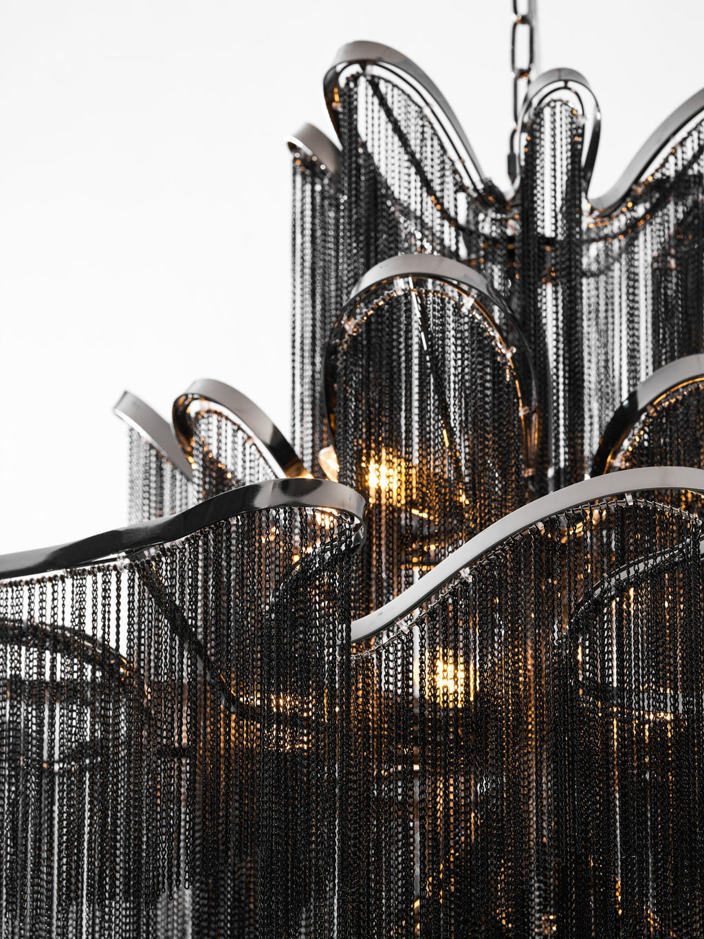 Close view of the black chain fringe and curved nickel frame on this lit Clérachic chandelier, bulbs glowing within.