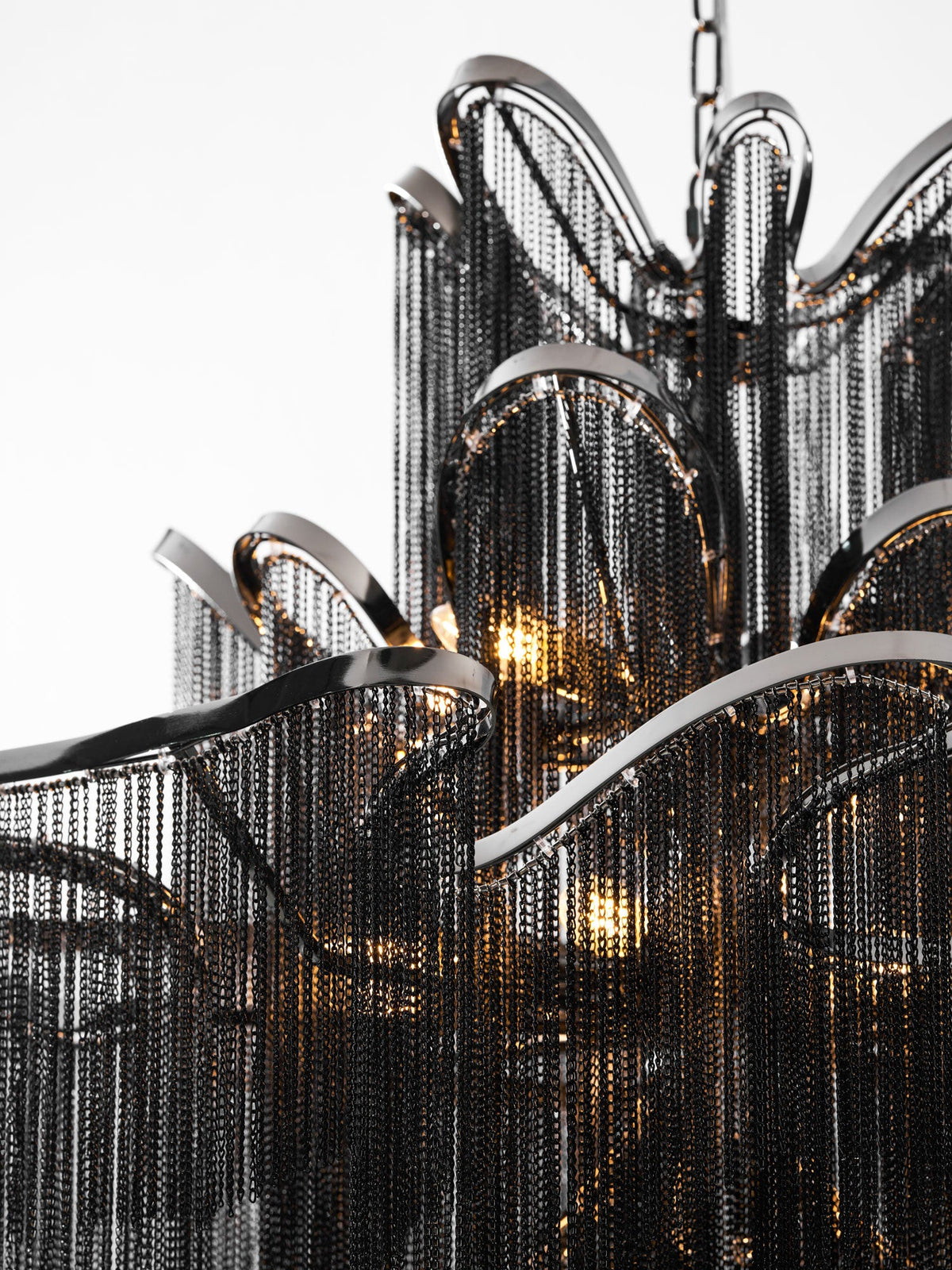 Close view of the black chain fringe and curved nickel frame on this lit Clérachic chandelier, bulbs glowing within.