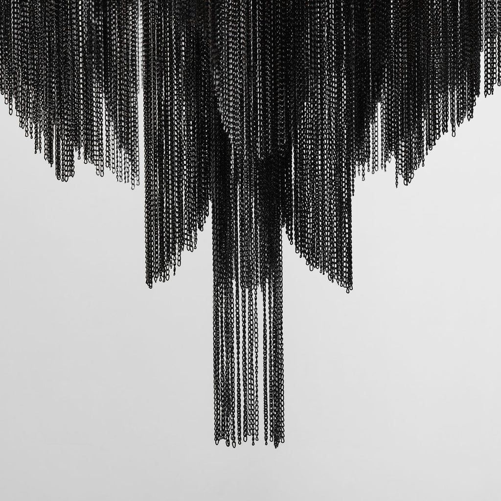 Black chain fringe cascades from this Clérachic chandelier down a plain white wall, with no frame or bulbs in view.