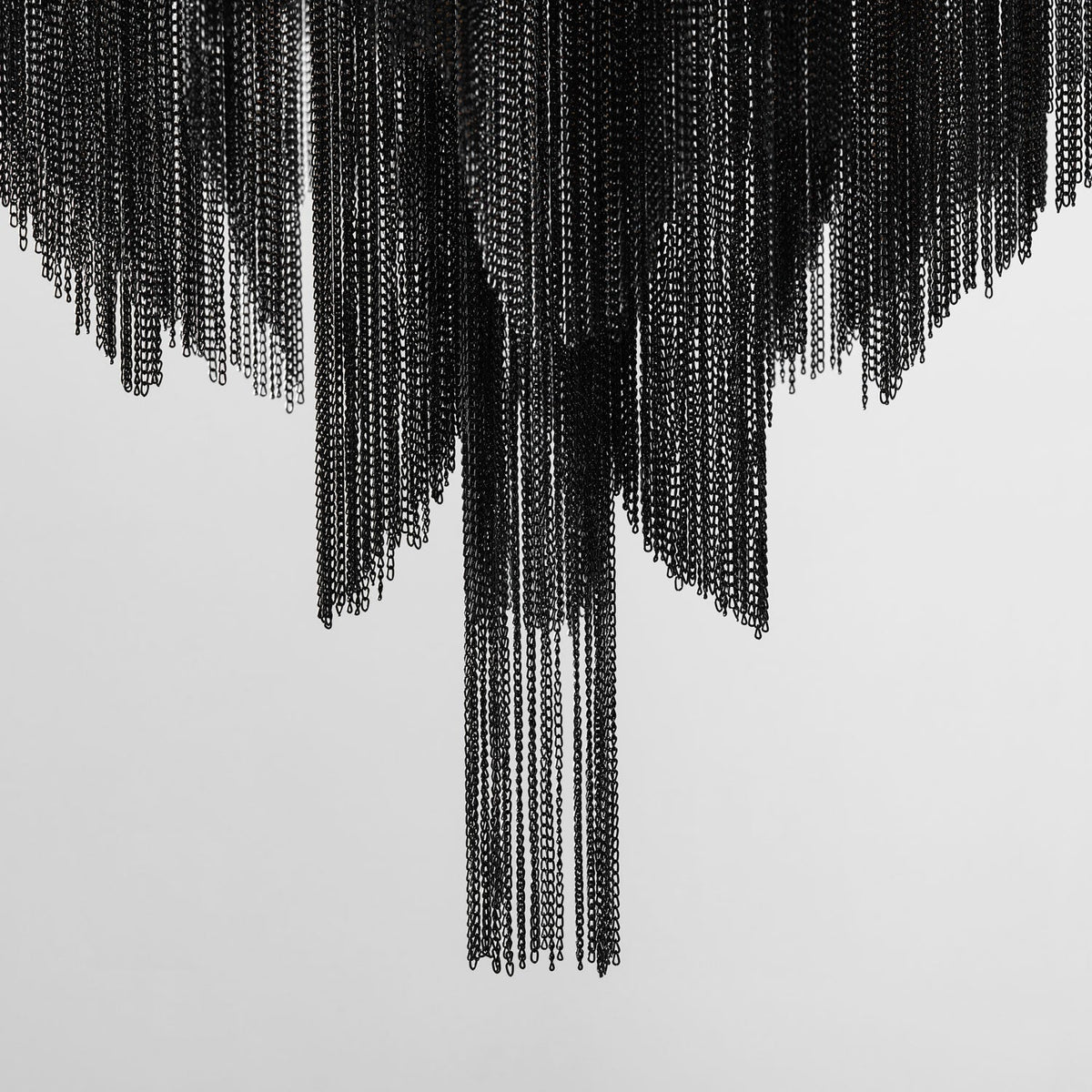 Black chain fringe cascades from this Clérachic chandelier down a plain white wall, with no frame or bulbs in view.