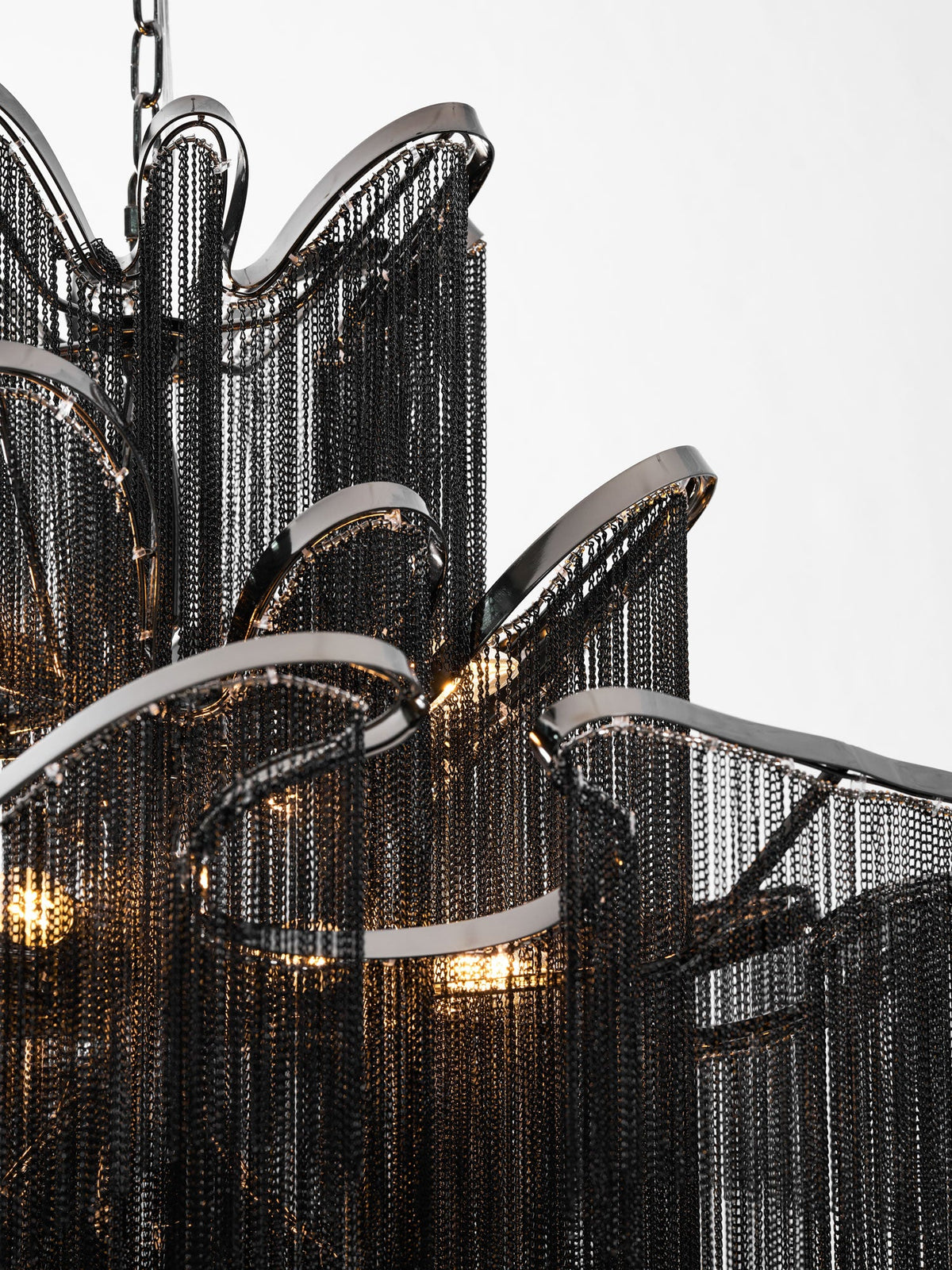 Close view of the curled black chain tiers and nickel arches on this lit Clérachic chandelier.