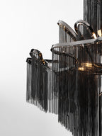 A tight close-up shows the black chain fringe spilling from curved nickel rods on this lit Clérachic chandelier.