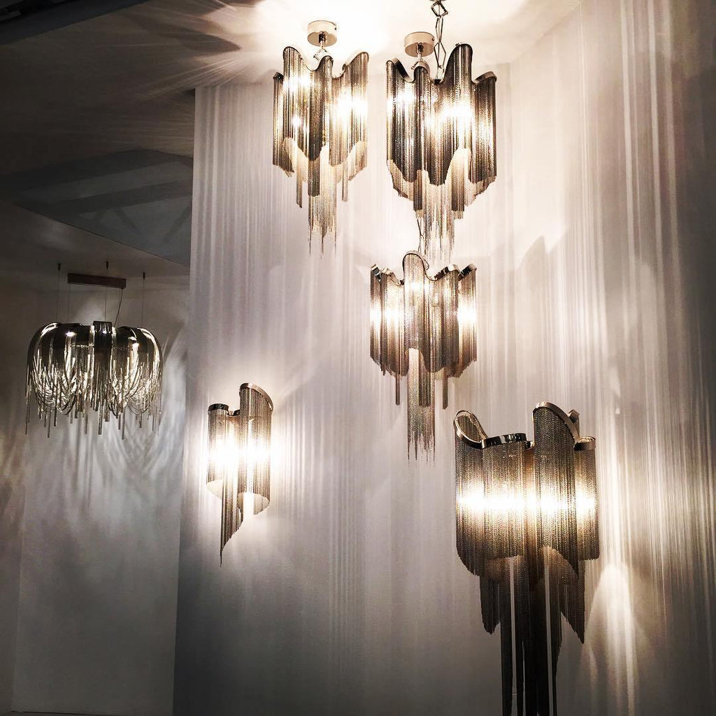Several sizes of this silver Clérachic chandelier hang lit together in a stairwell, framed by sheer white drapery.