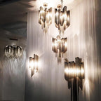 Several sizes of this silver Clérachic chandelier hang lit together in a stairwell, framed by sheer white drapery.