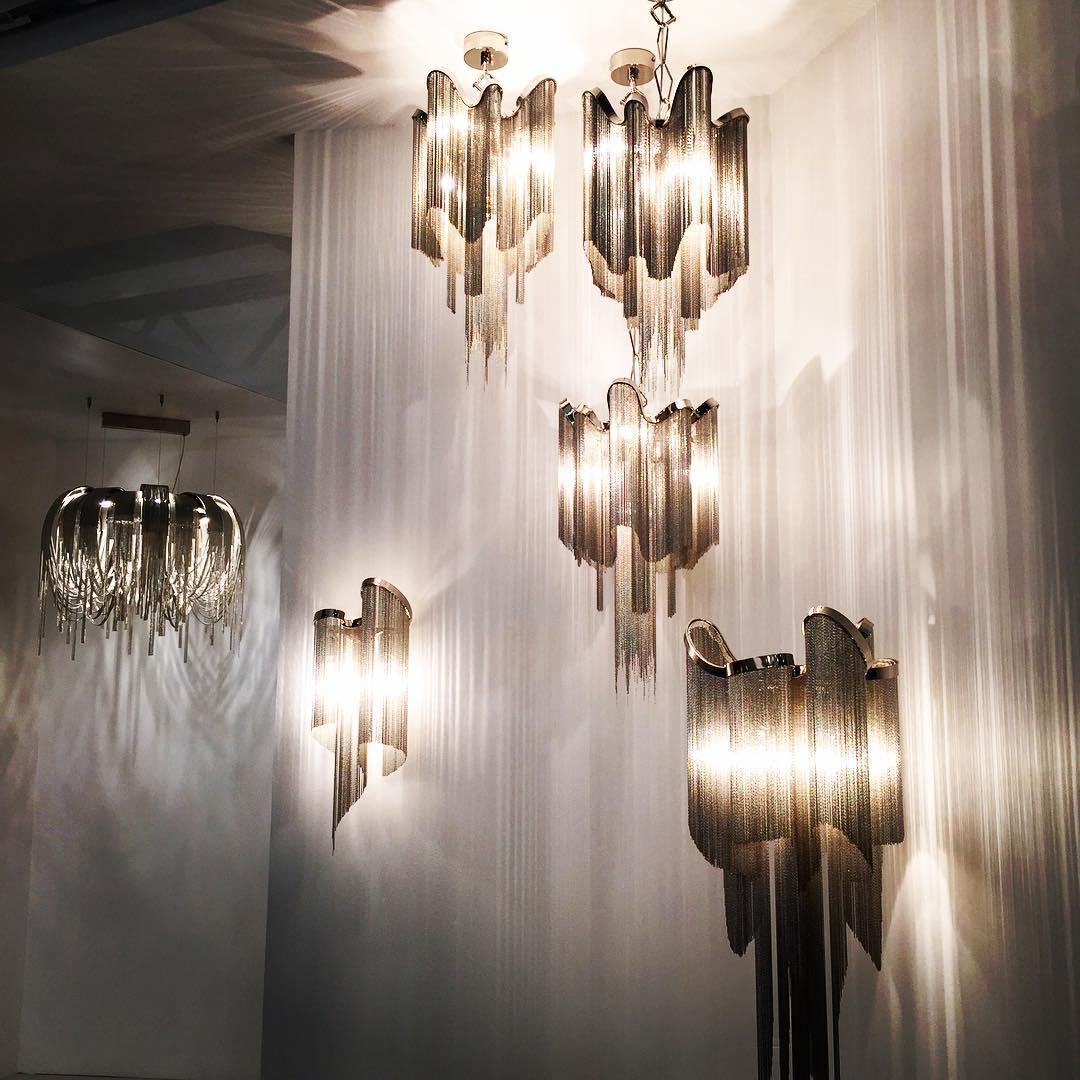 Several sizes of this silver Clérachic chandelier hang lit together in a stairwell, framed by sheer white drapery.