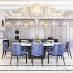 Above a long marble dining table with blue upholstered chairs, this lit Clérachic chandelier hangs with pale chain fringe and a gold-rimmed frame.
