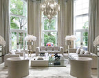 Floor-to-ceiling windows and feather centrepieces frame this lit silver Clérachic chandelier in a tall living room.