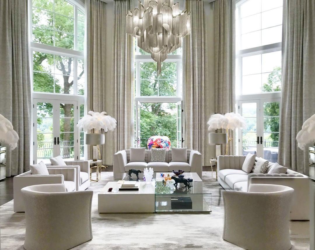 Floor-to-ceiling windows and feather centrepieces frame this lit silver Clérachic chandelier in a tall living room.